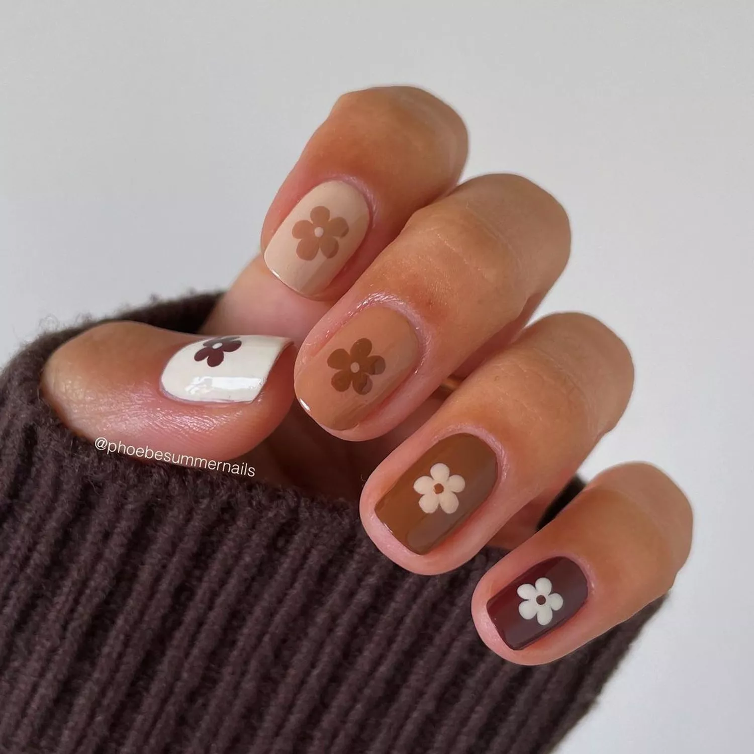 A manicure in various shades of brown, with daisies (also in shades of brown) on each finger