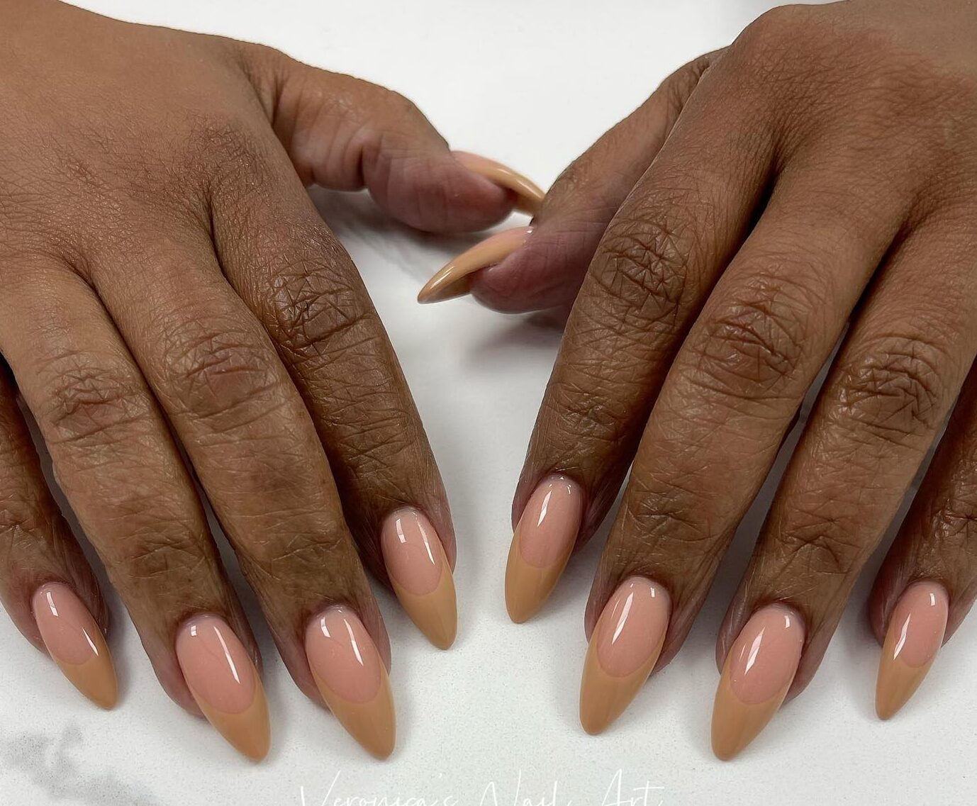 Nude nail color with pale brown French tips on long almond shaped acrylic nails