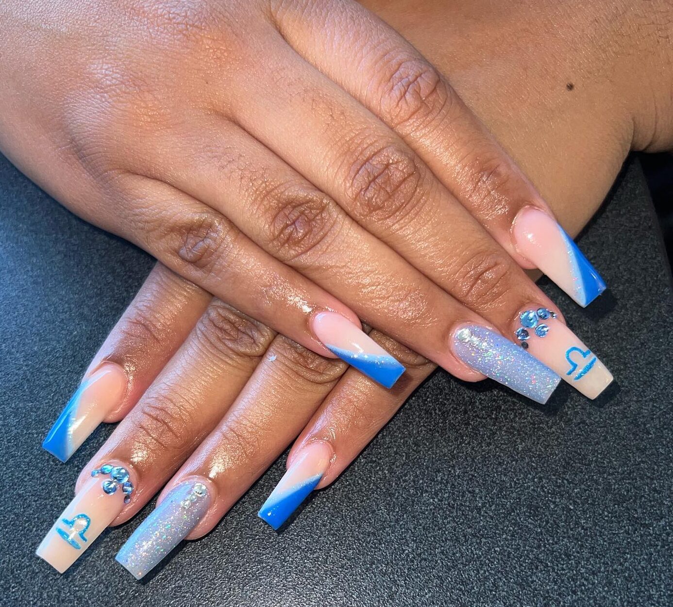 Nude nail color with blue slanted French tips, Libra sign, and rhinestones nail designs on long square shaped acrylic nails