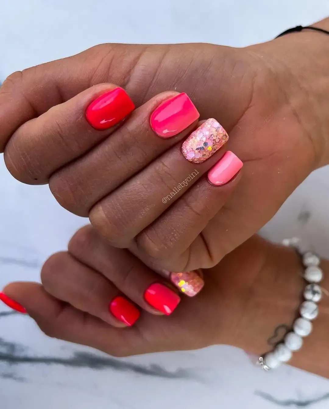 Short neon pink nails with glitter.