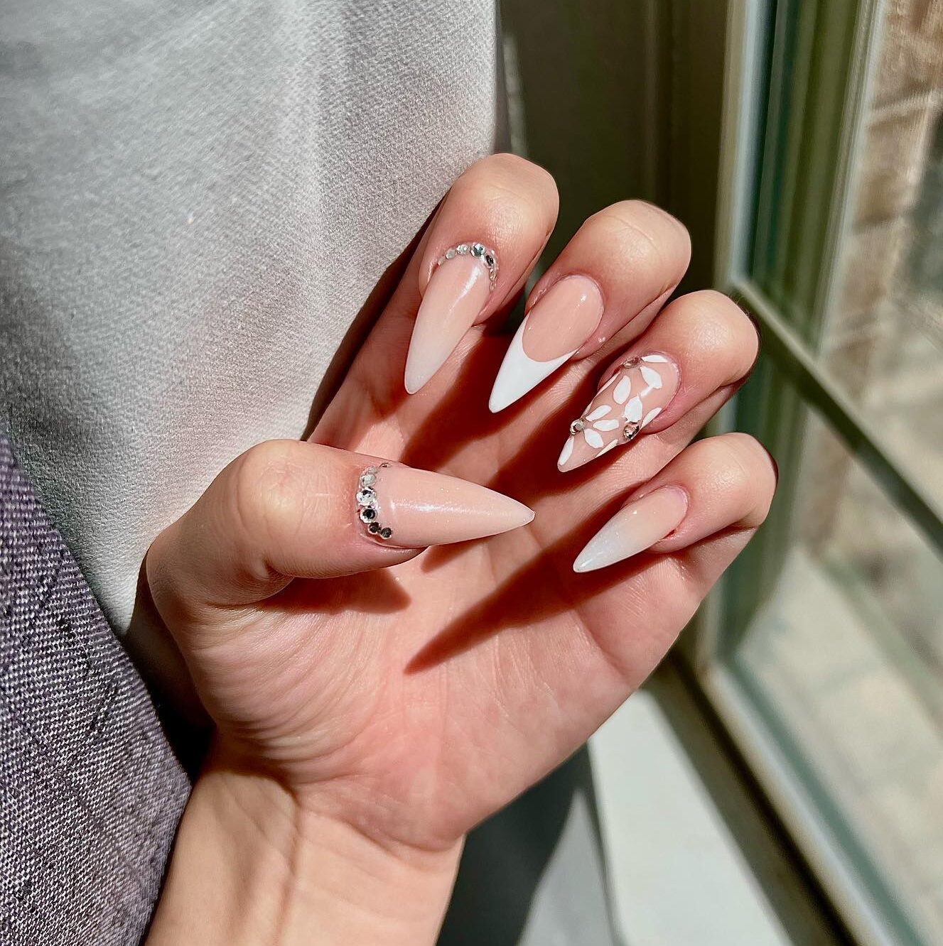 Nude nail polish with white tips, white floral designs, and rhinestones on long stiletto nails