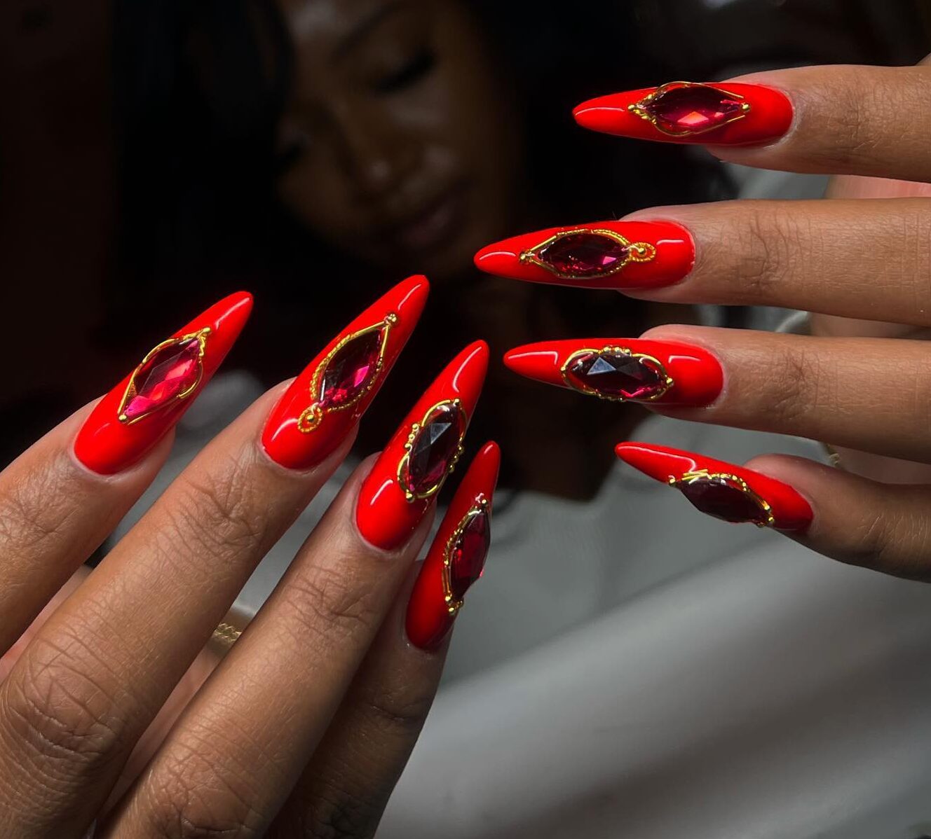 Vibrant red nail polish with red gems on long stiletto nails